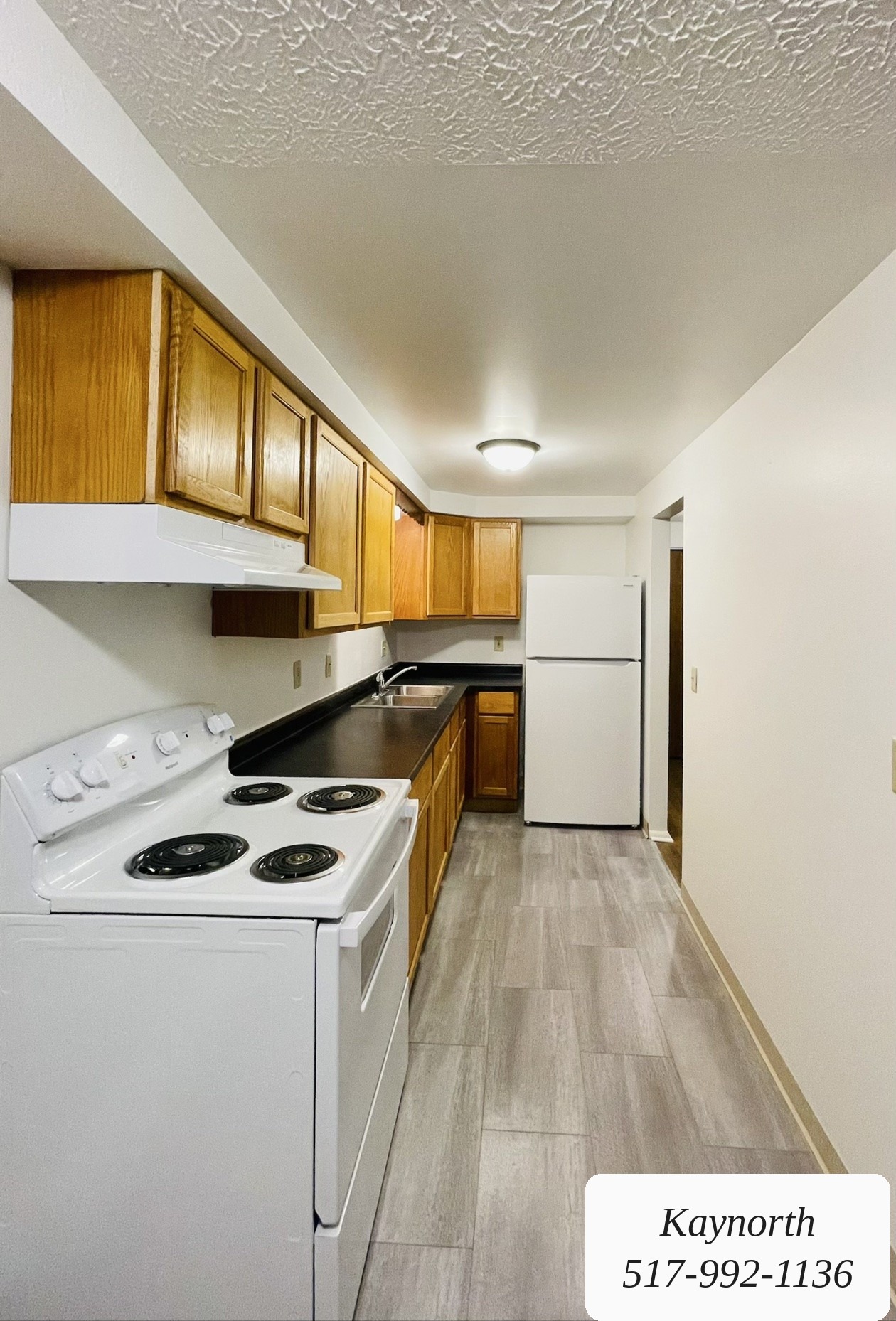 Galley kitchen with wood cabinets, range, and refrigerator in a Kaynorth apartment